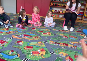 Dzieci na dywanie wraz z rodzicem słuchają czytanej książki
